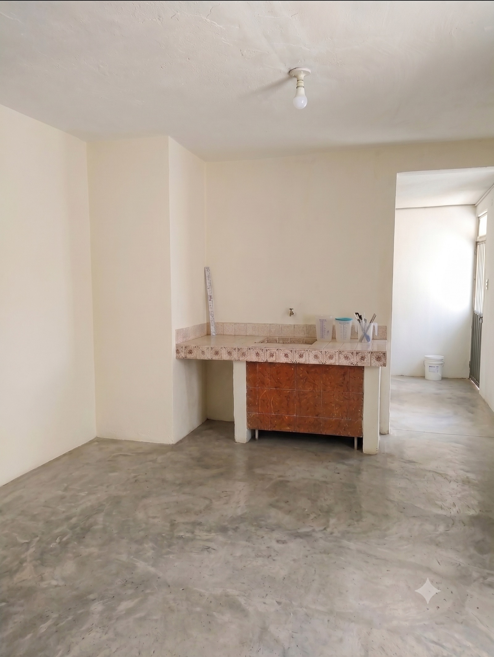 Área con barra tipo cocineta, muros claros y piso de concreto pulido