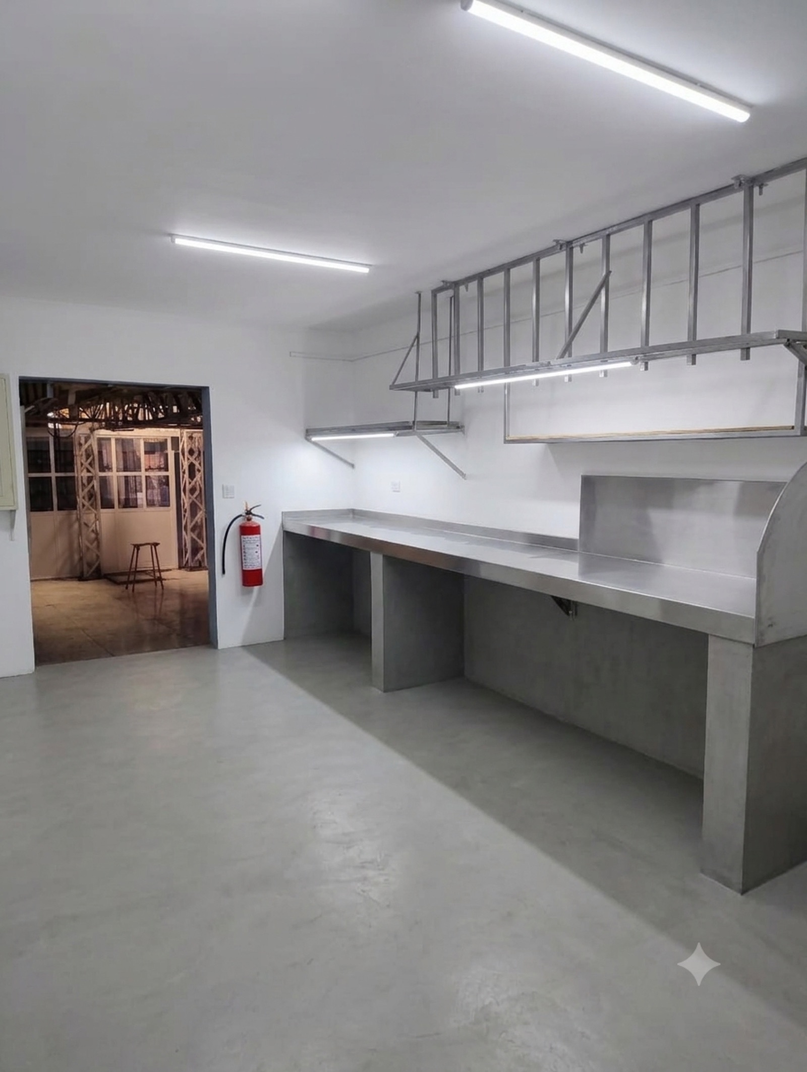 Área de trabajo con mesas de acero, estantería colgante y muros blancos