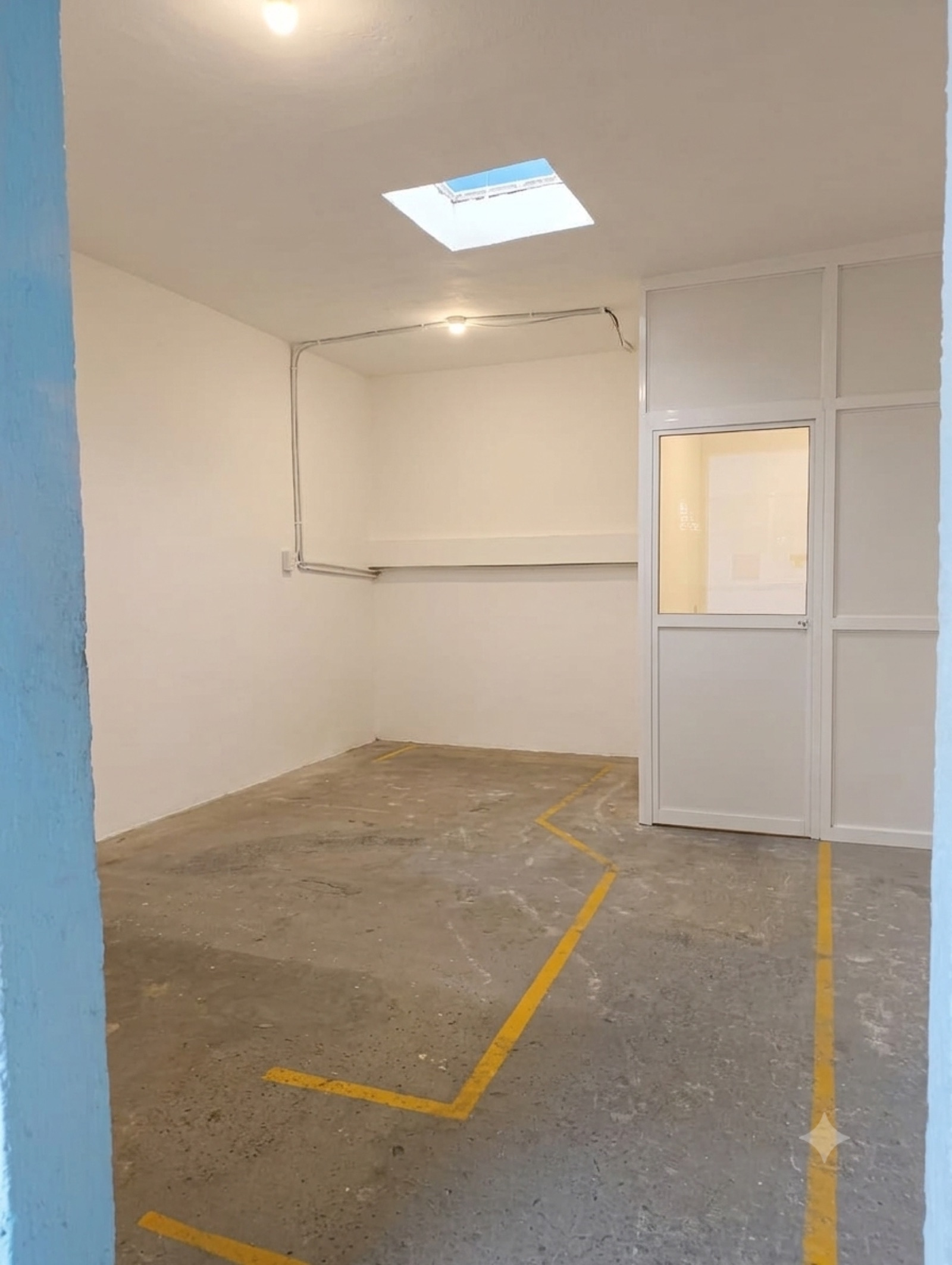 Cuarto con tragaluz, muros divisorios blancos y piso marcado con línea amarilla