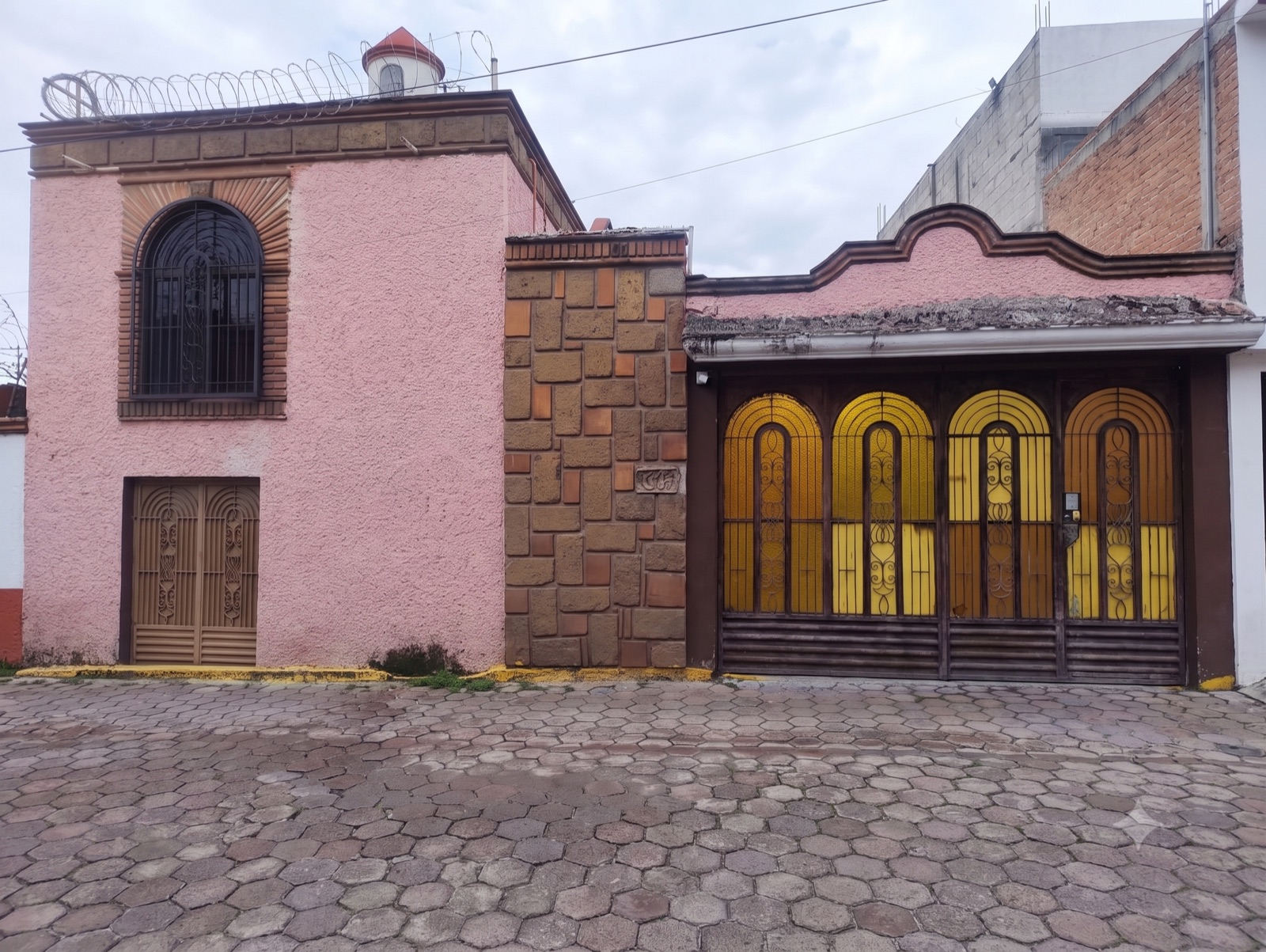 Fachada exterior con torre, ventana de arco con herrería, muro de piedra y portón amarillo con arcos