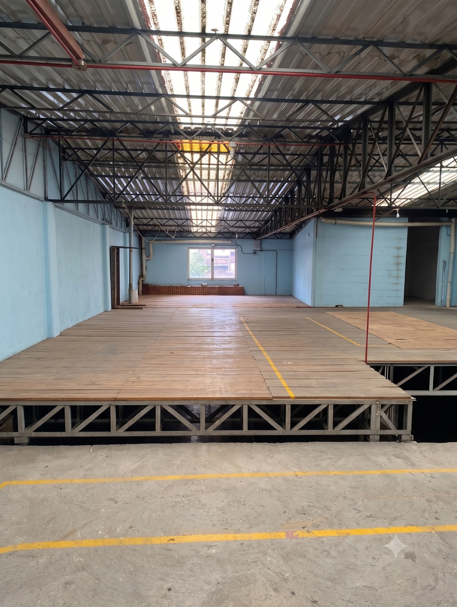 Nave principal con estructura metálica, techo con láminas translúcidas y tarimas de madera sobre el piso