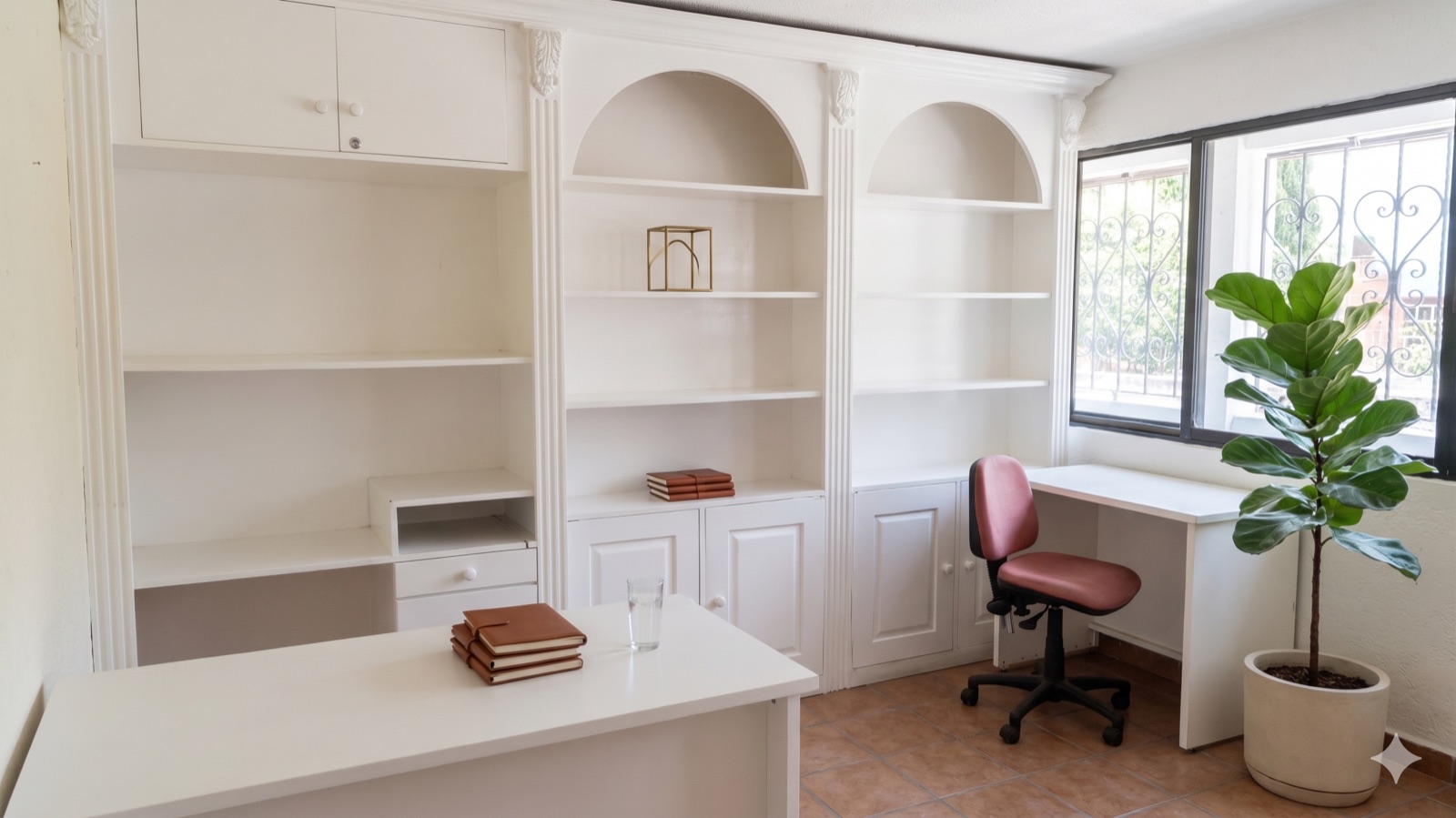 Oficina blanca con libreros de arco, escritorio y silla, ventana con herrería