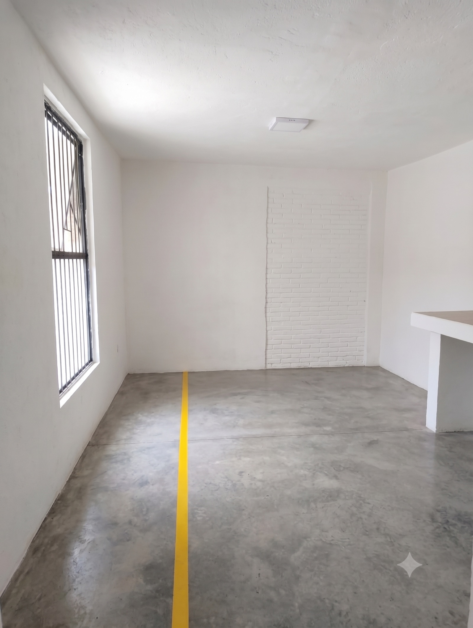 Cuarto vacío con muros blancos, piso de concreto pintado y ventana con herrería