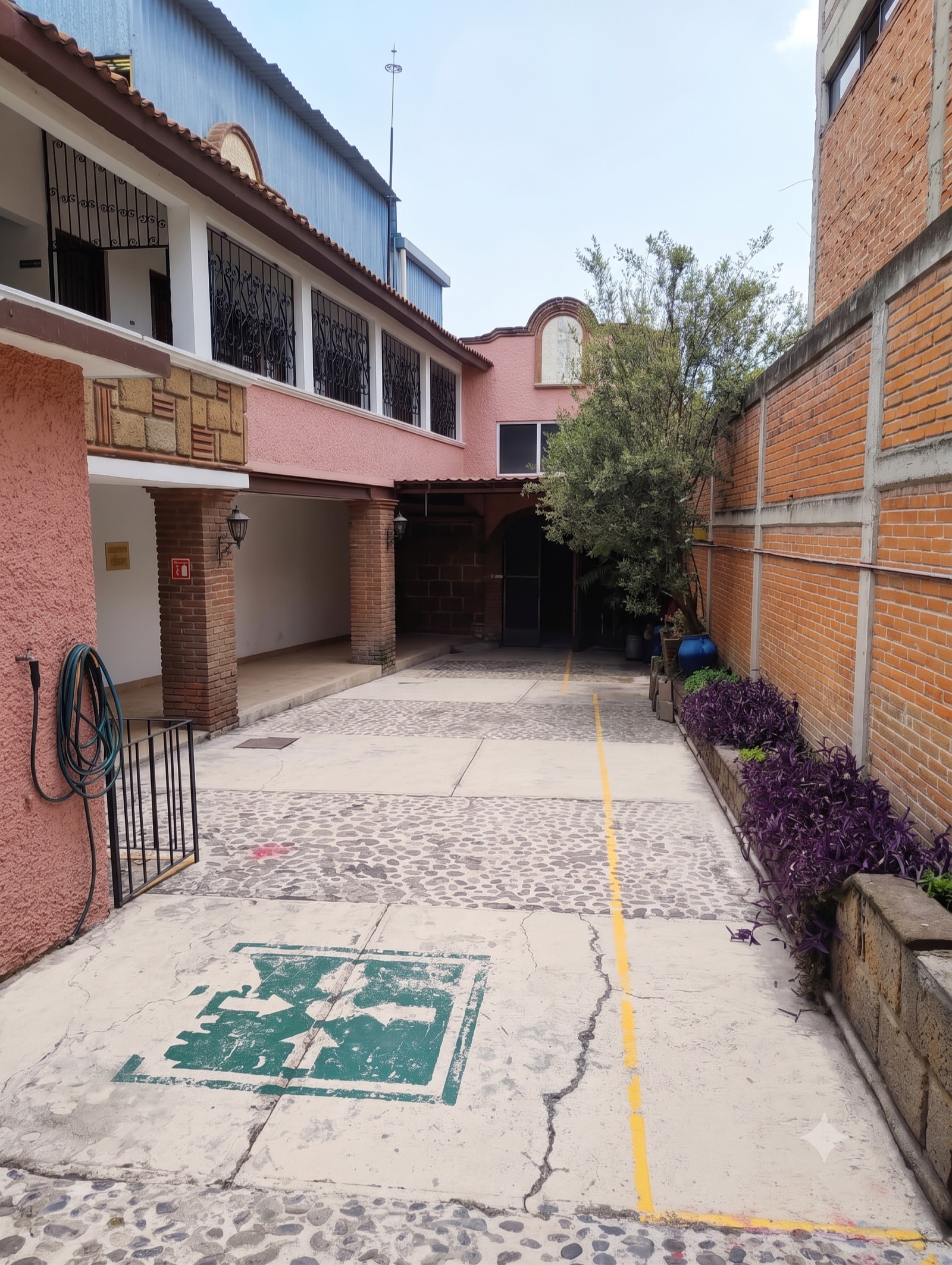 Patio lateral empedrado con casa color rosa, arcos y muro de ladrillo aparente