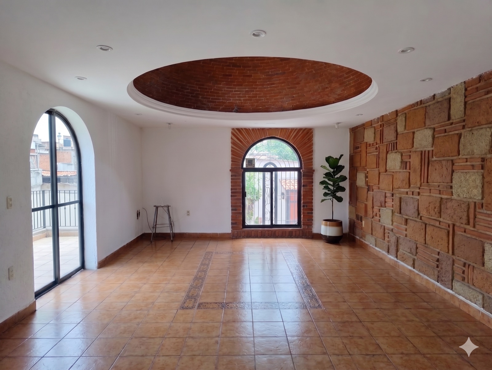 Sala con domo circular de tabique aparente, ventanas de arco y muro de piedra decorativa